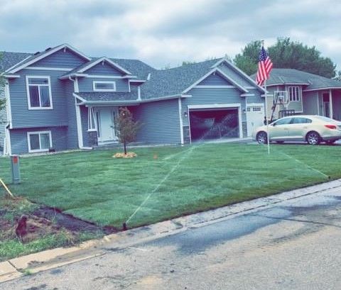 Suburban house with a green lawn, American flag, and white car parked in the driveway.