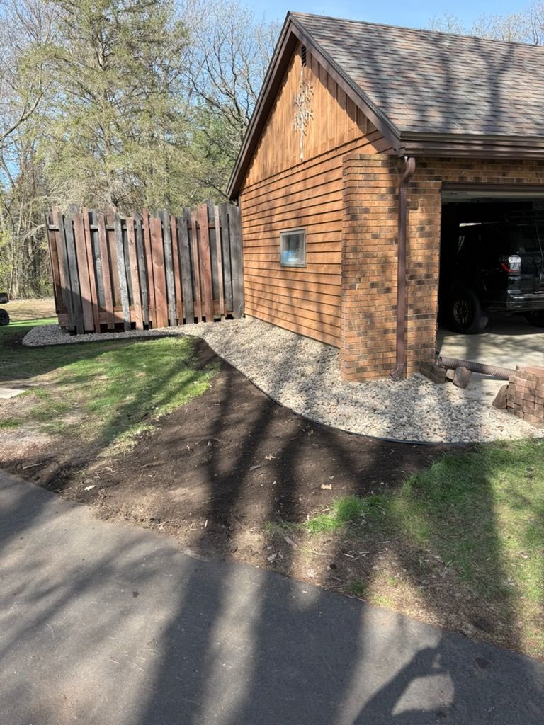 Brick garage with gravel edging, wooden fence, and tree shadows beside a driveway