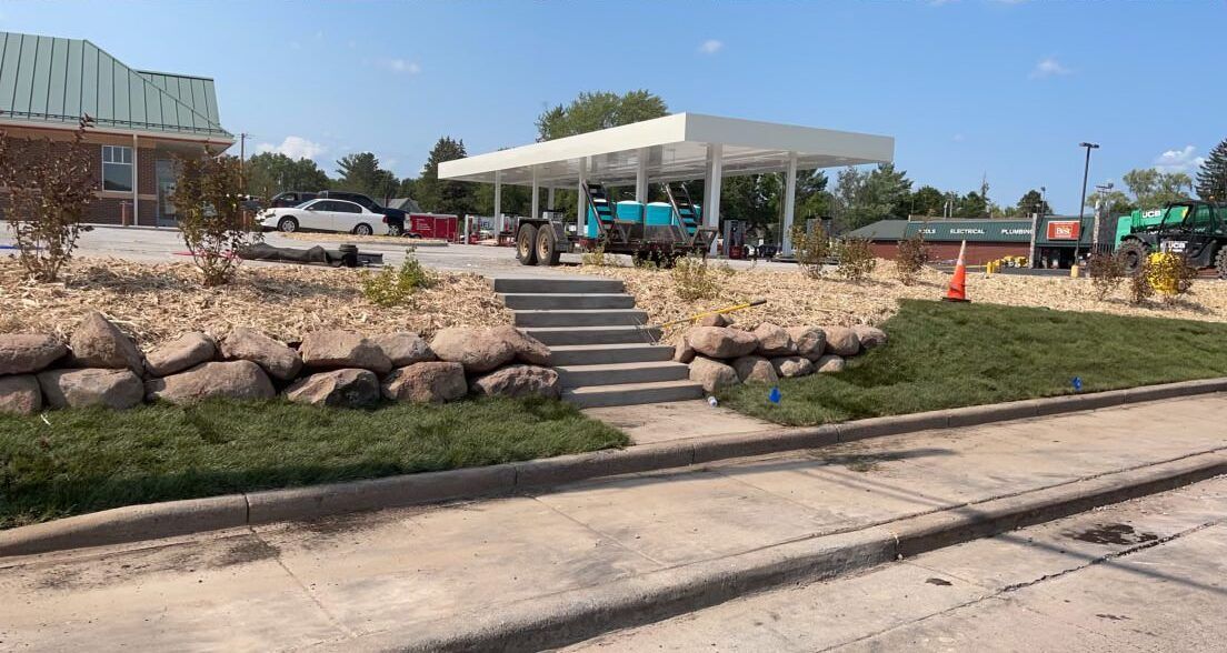 Outdoor café pavilion by a roadside with stone steps, rocks, and clear blue sky.