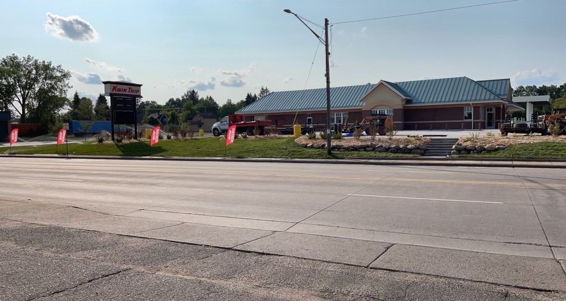 Roadside view of a low building with a green roof, flags, and a sign under a partly cloudy sky.