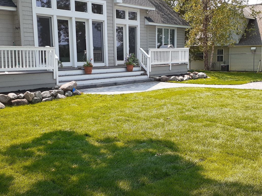 White house with porch and stone steps, front lawn, and a person standing by the entrance.