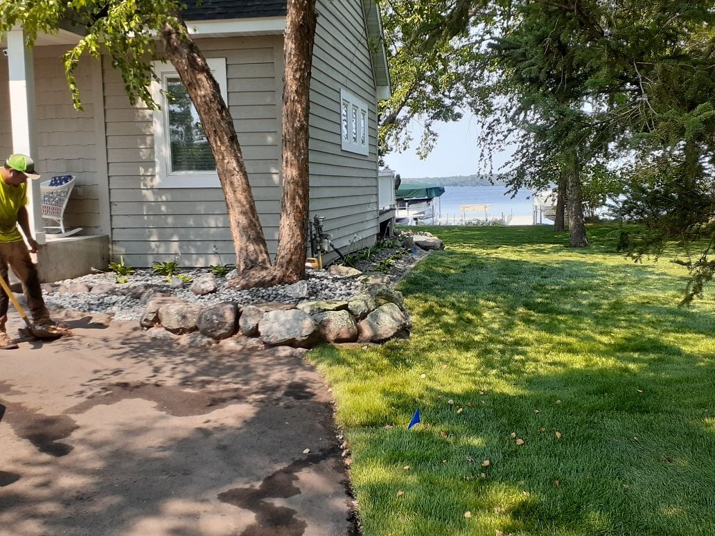 House by lakeside lawn with stone border and trees, viewed from a paved patio