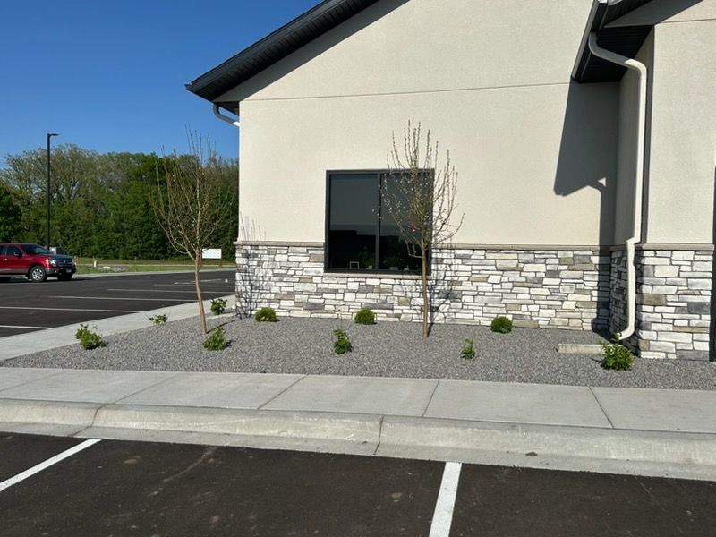 Exterior of a building with stone facade, window, sidewalk, and parking lot under clear skies