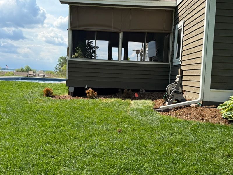 Backyard patio with screened porch, green lawn, and cloudy sky over water.