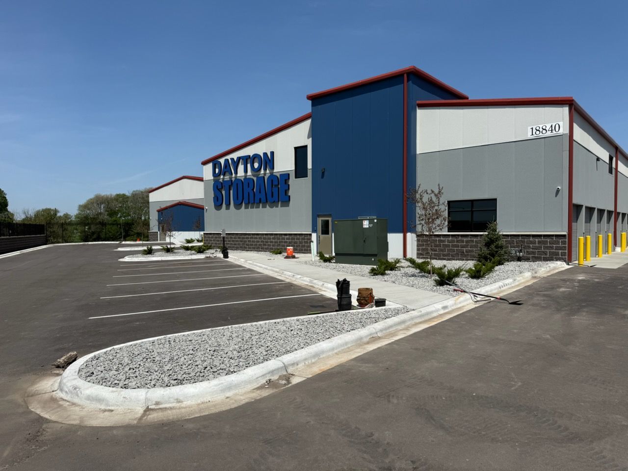 Exterior of a blue-and-gray commercial building with a large paved parking lot and clear sky