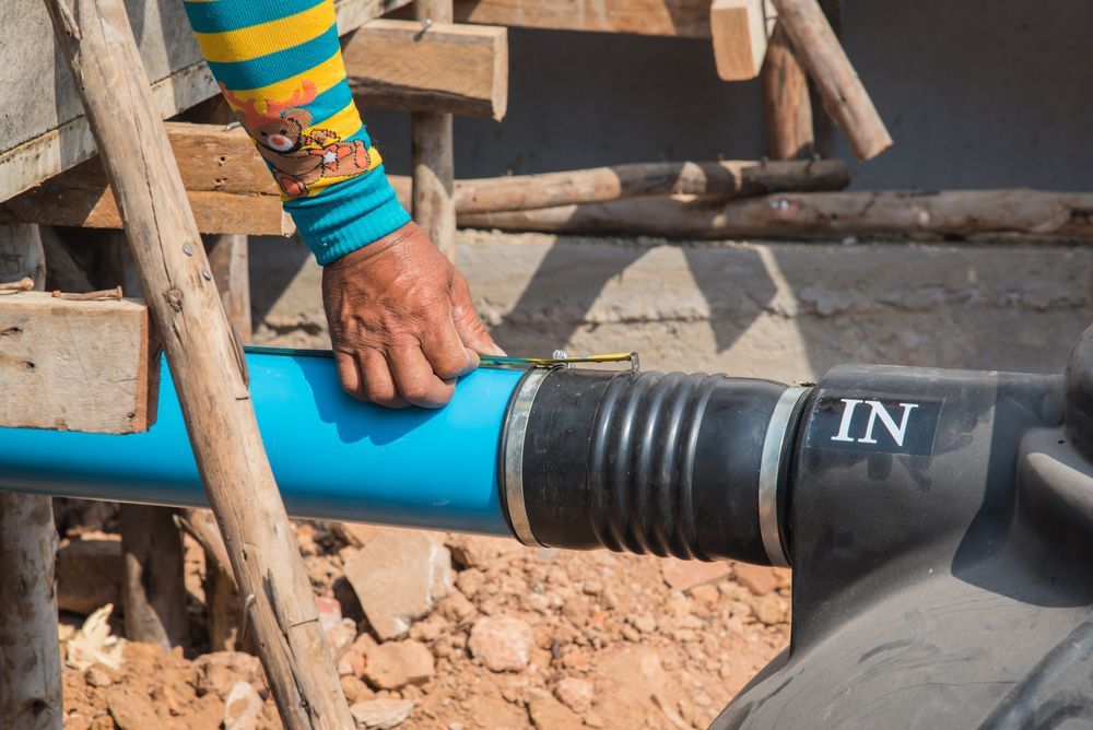 Person connecting blue pipe to a black tank, labeled 