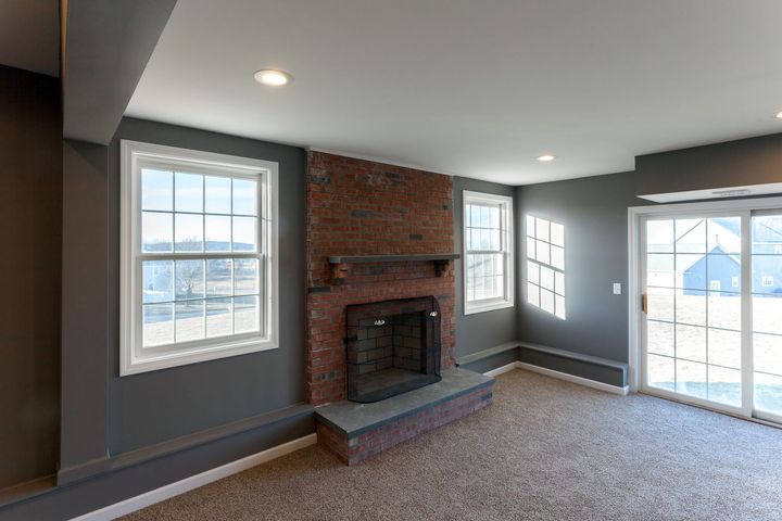 Empty living room with gray walls, carpet, brick fireplace, and large windows with snowy outdoor view