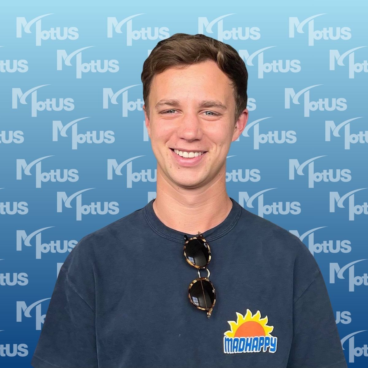 Four smiling colleagues posing with thumbs up in front of a blue Motus backdrop