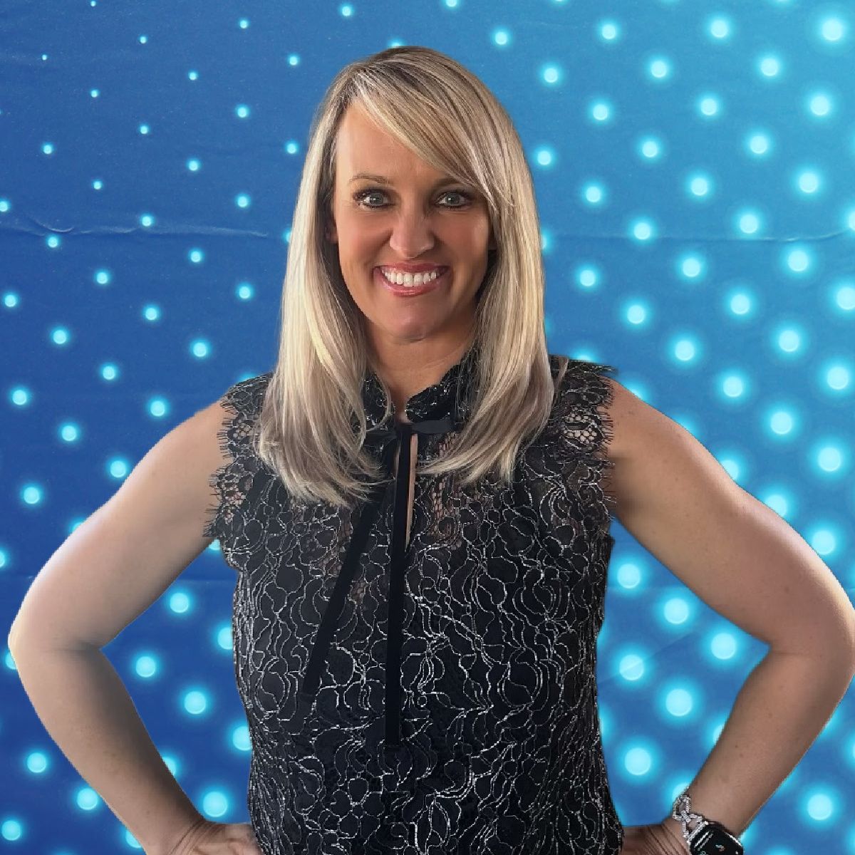 Smiling blonde woman in a black sleeveless top, standing with hands on hips against a blue dotted background