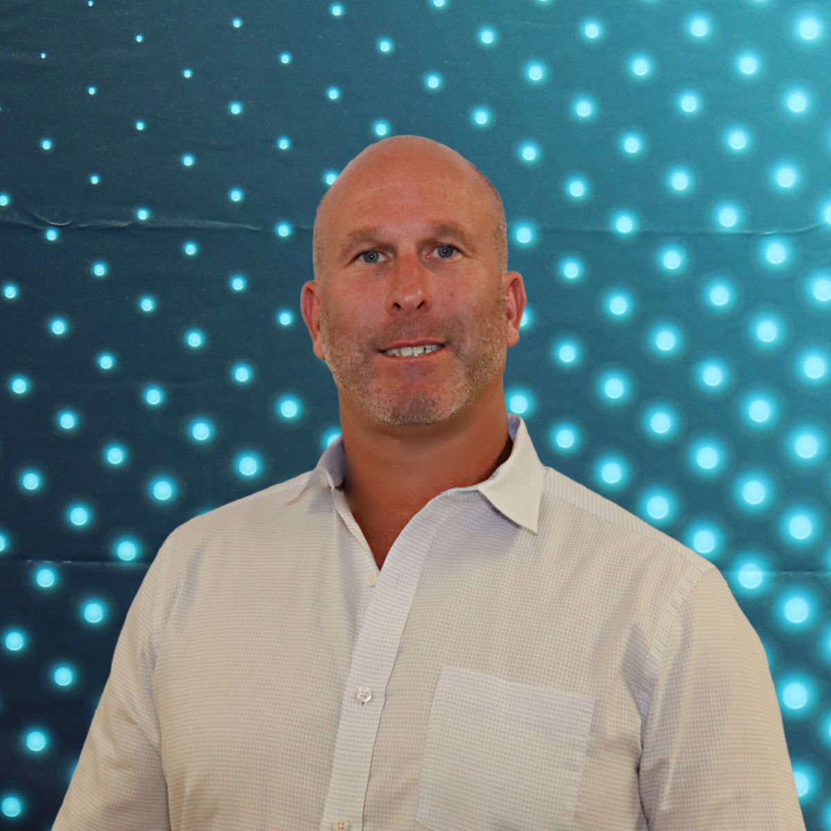 Man standing in a white shirt against a blue dotted light display background