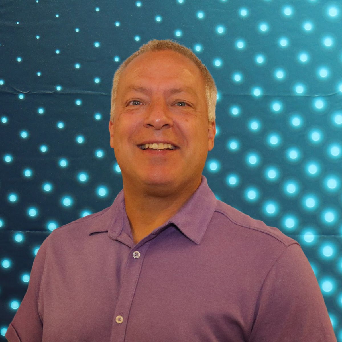 Smiling man in a purple shirt against a blue dotted light background