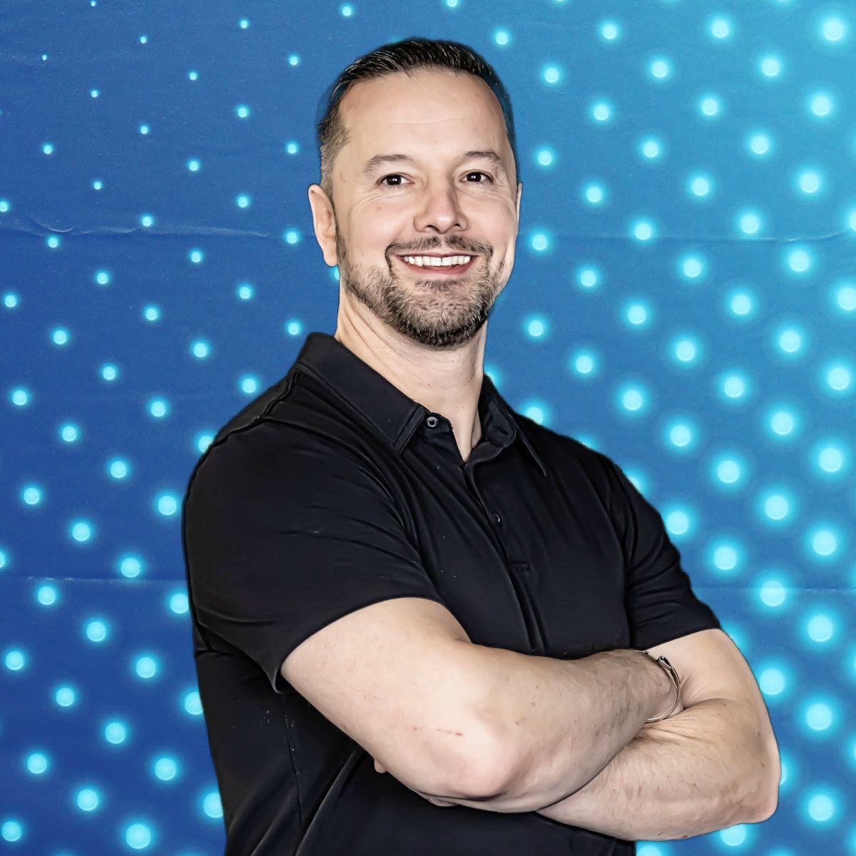 Smiling man in a black polo with arms crossed against a blue dotted background