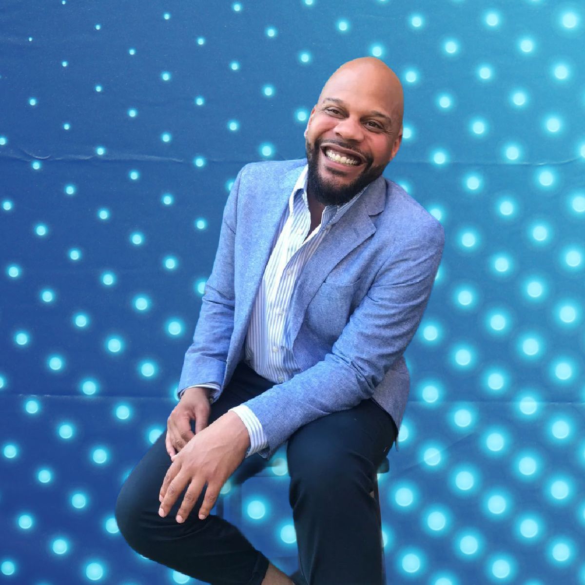 Smiling man in a blue blazer and tie seated against a blue dotted light backdrop
