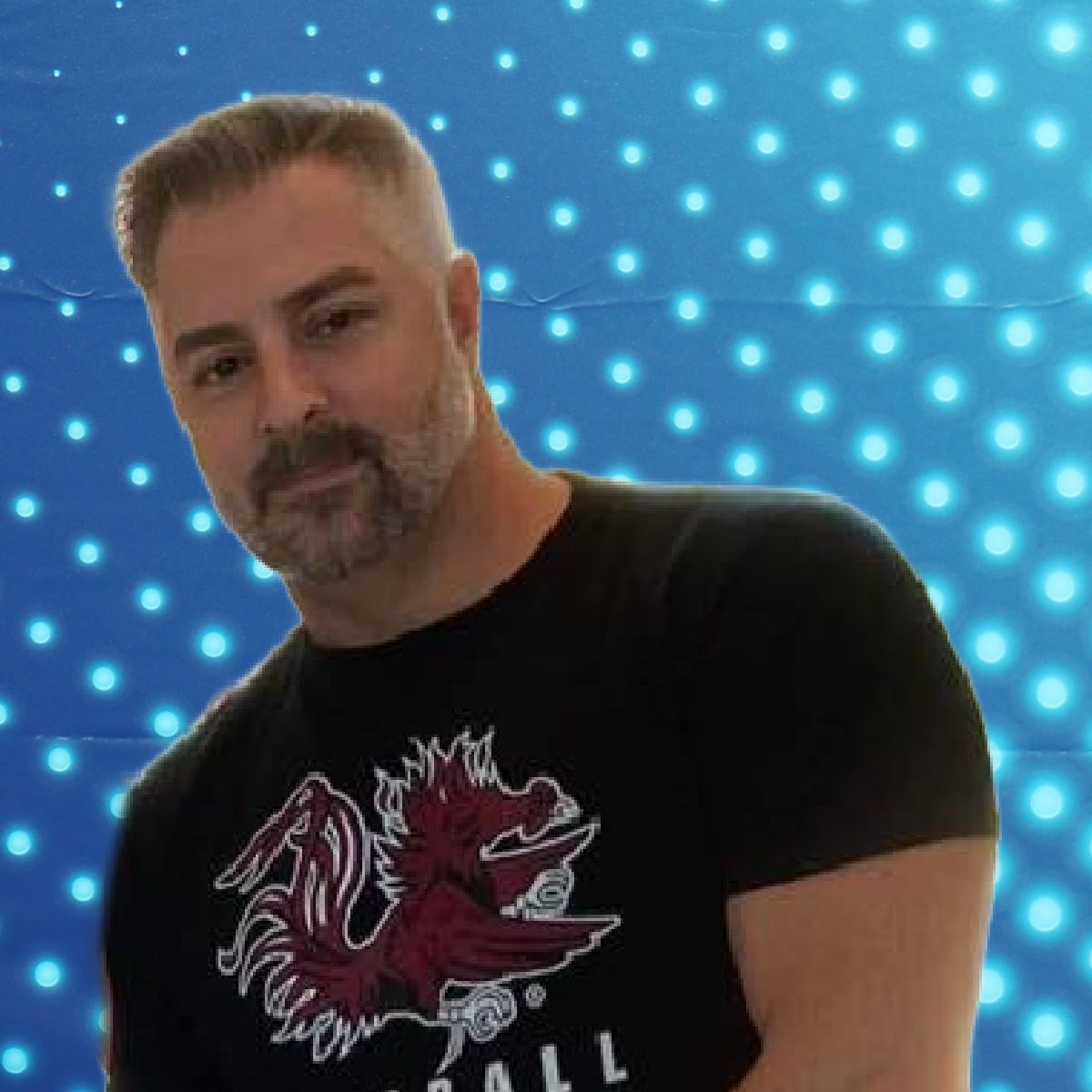 Man in black T-shirt with red graphic, standing before a blue dotted light background.