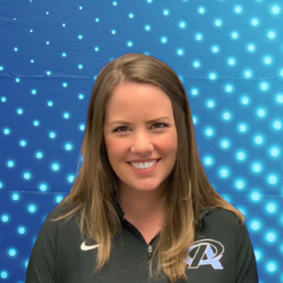 Smiling person in a black polo standing before a blue dotted backdrop