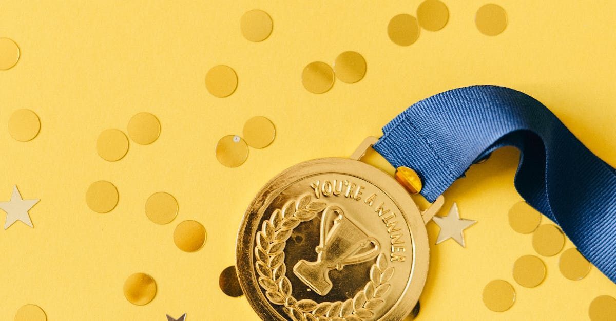 Gold medal with blue ribbon on a yellow background, surrounded by confetti-like dots.