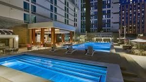 Hotel courtyard pool area with glowing blue hot tubs, lounge chairs, and surrounding high-rise buildings at dusk