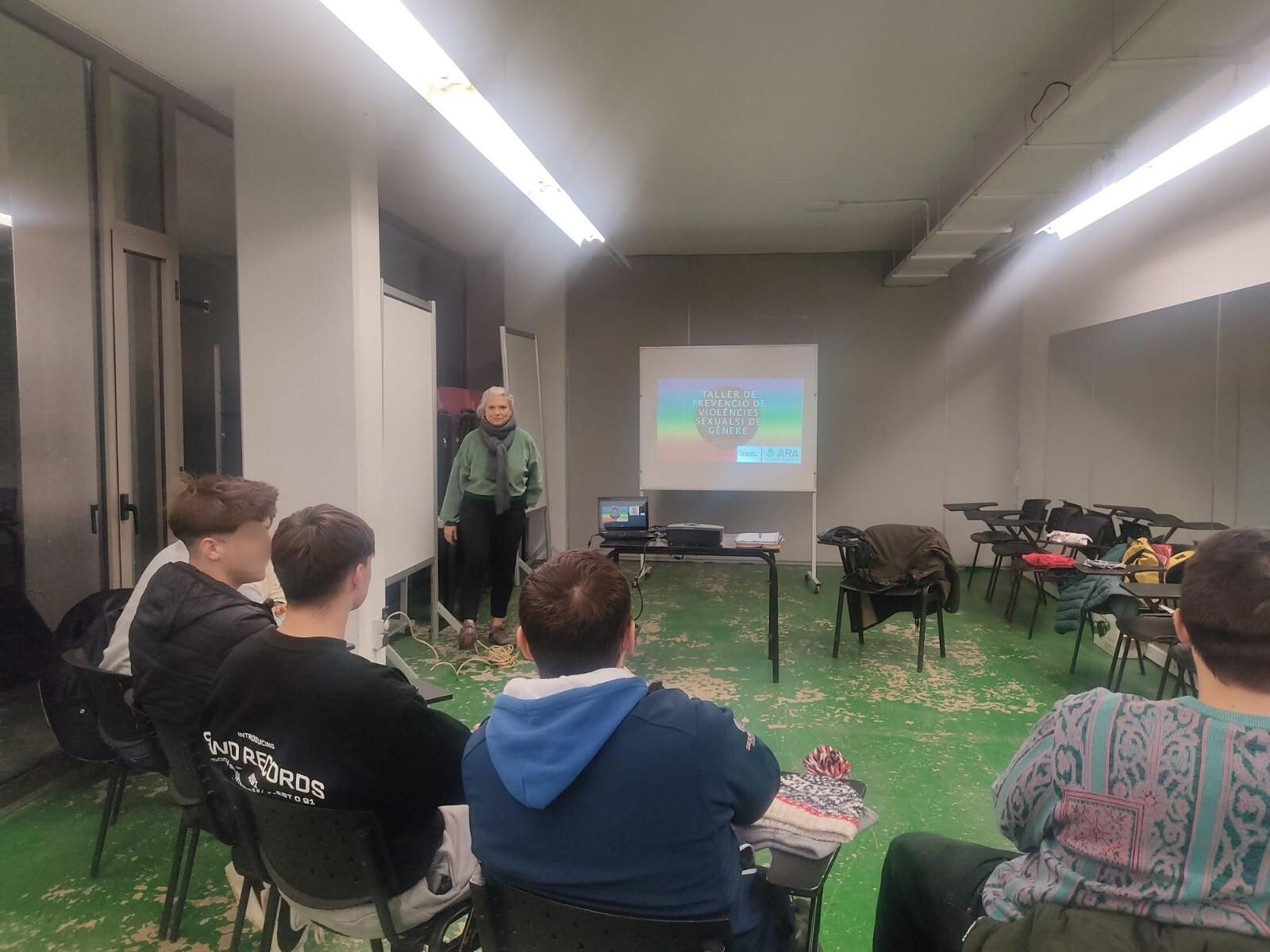 Una persona fa una presentació a un grup petit en una sala amb una pantalla de projector.