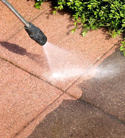 A person is using a high pressure washer to clean a brick walkway.