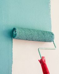 A paint roller is being used to paint a wall blue.