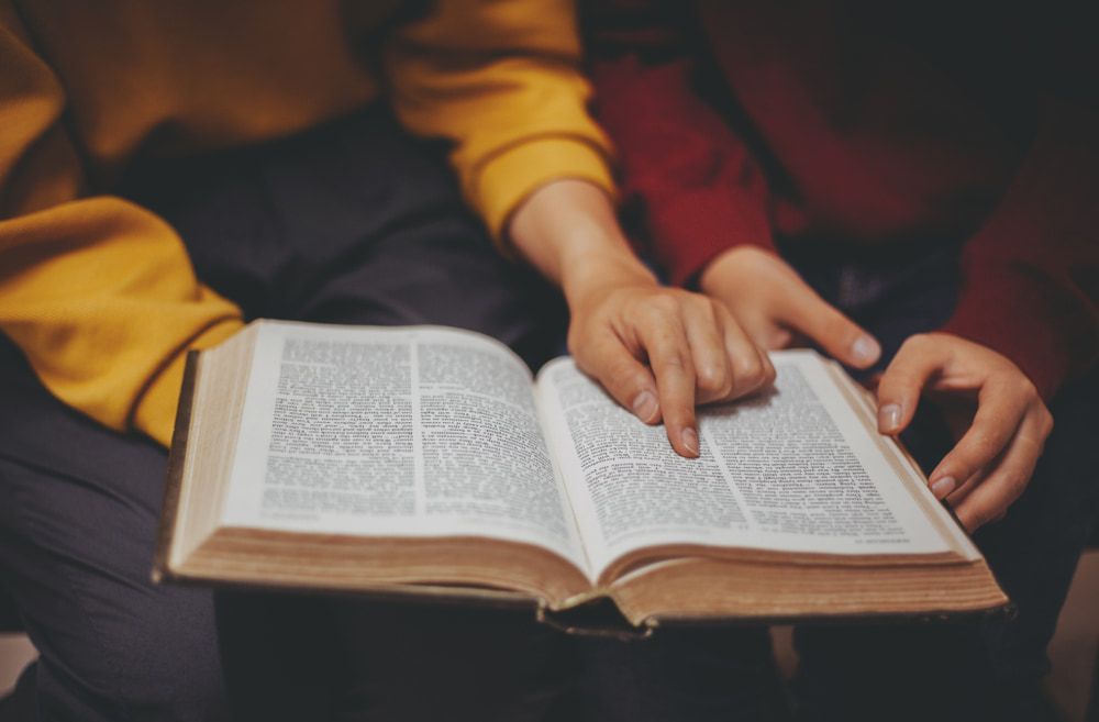 Two people reading an open book together, one pointing at text.