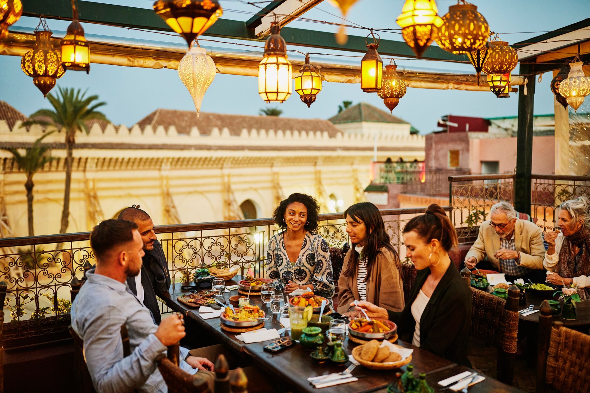 People dining outdoors at a rooftop restaurant, lanterns overhead.