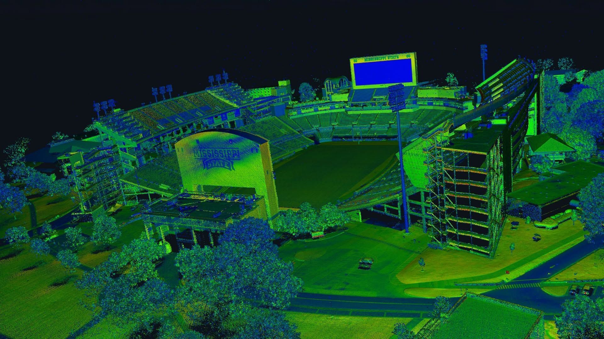 Colorful aerial view of a sports stadium with surrounding buildings and roads at night