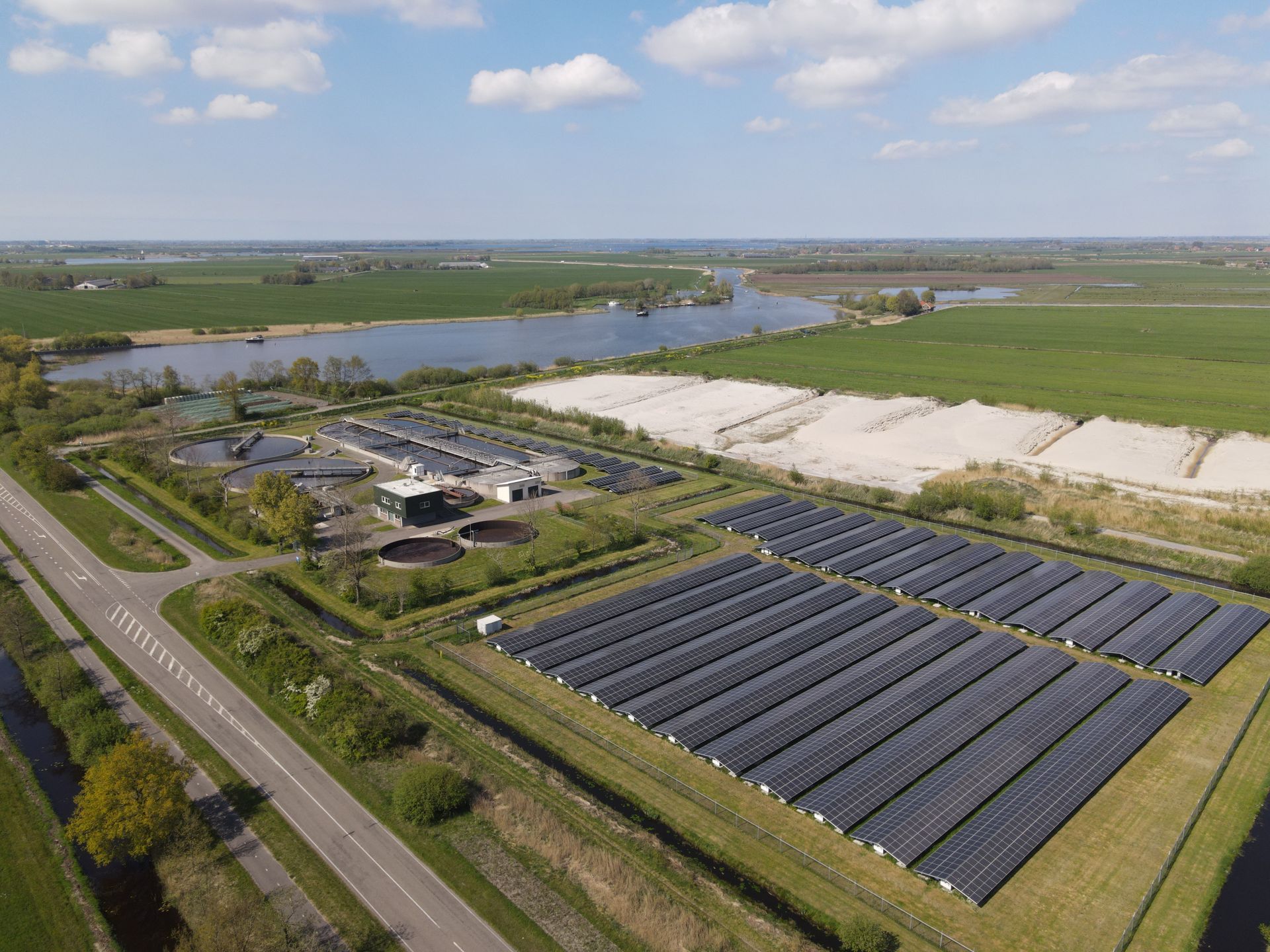 Aerial view of a solar farm beside a river and road in a rural landscape