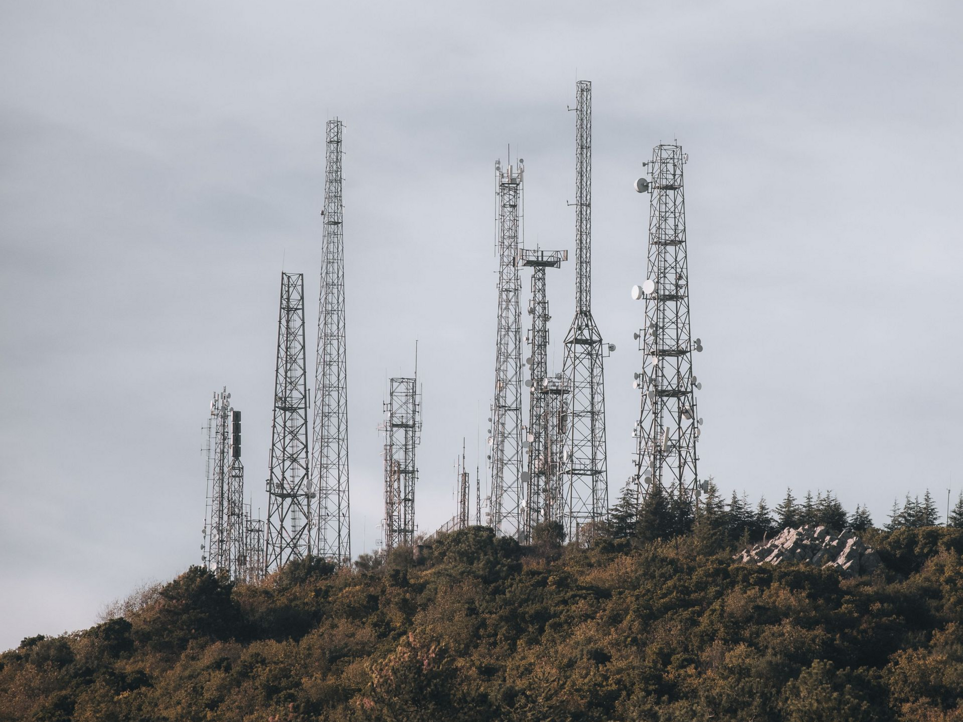 Several cell towers on a hill under a gray sky