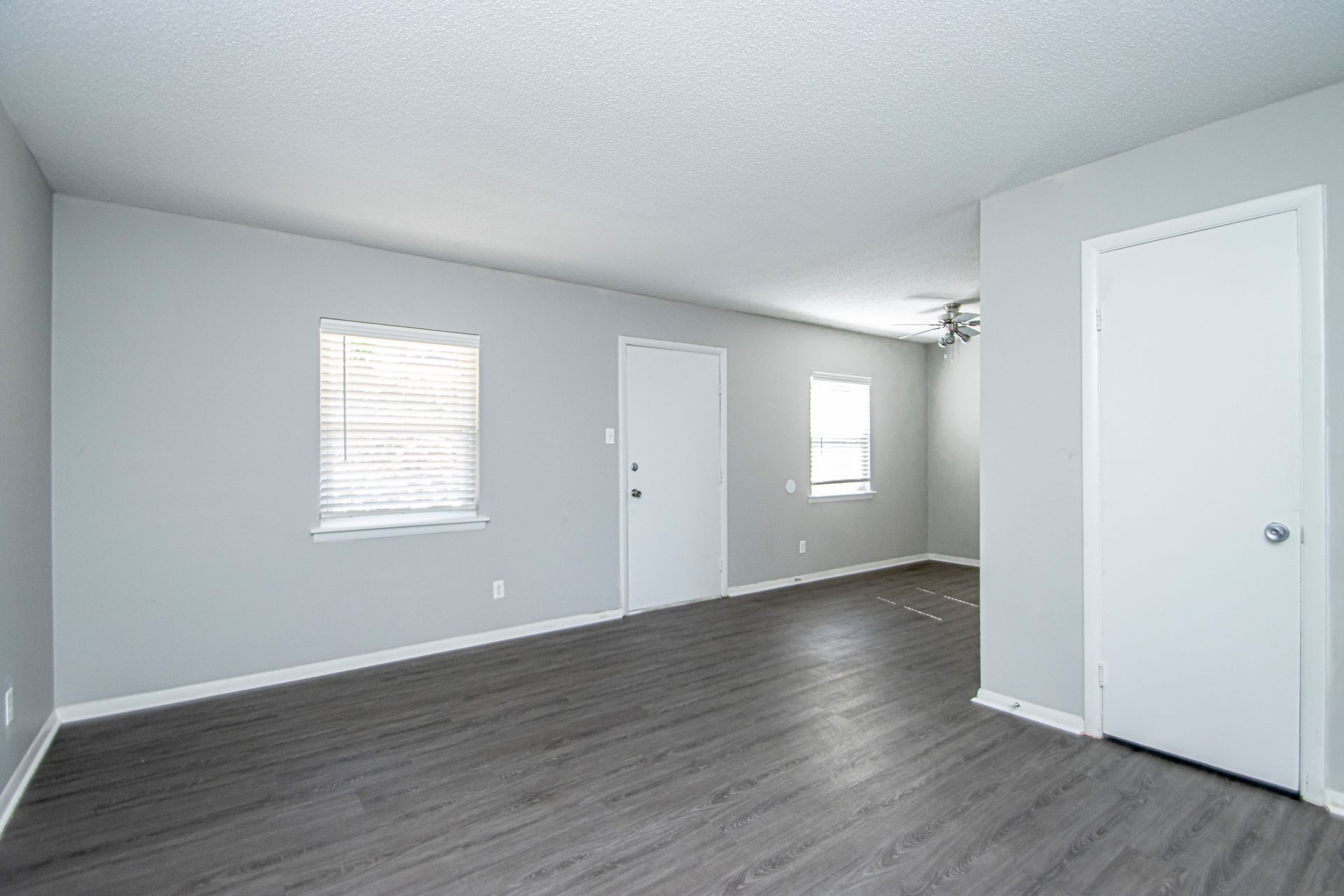 Empty room with gray walls, dark wood-look floor, white doors and trim, and two windows with blinds.
