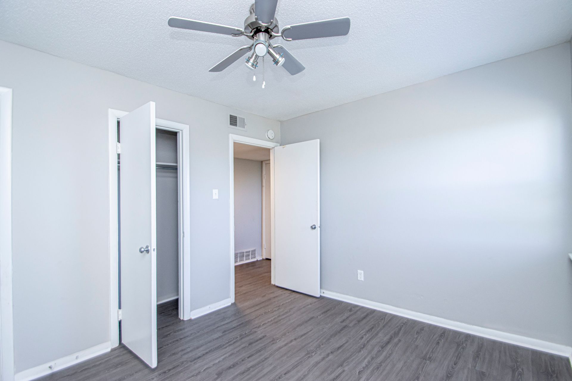 Empty bedroom with gray walls, closet, open door to another room, ceiling fan, and laminate flooring.