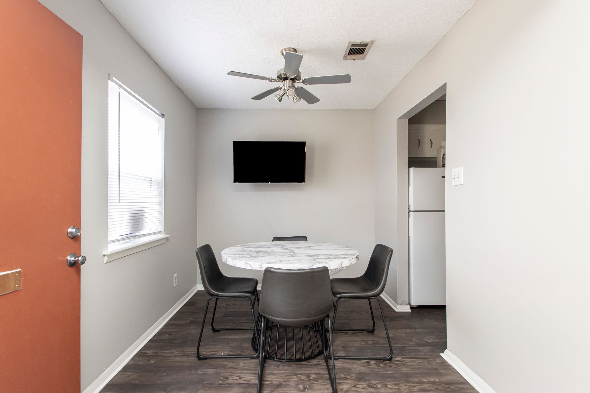 A dining area with a round table and four black chairs, a TV, and a white refrigerator.