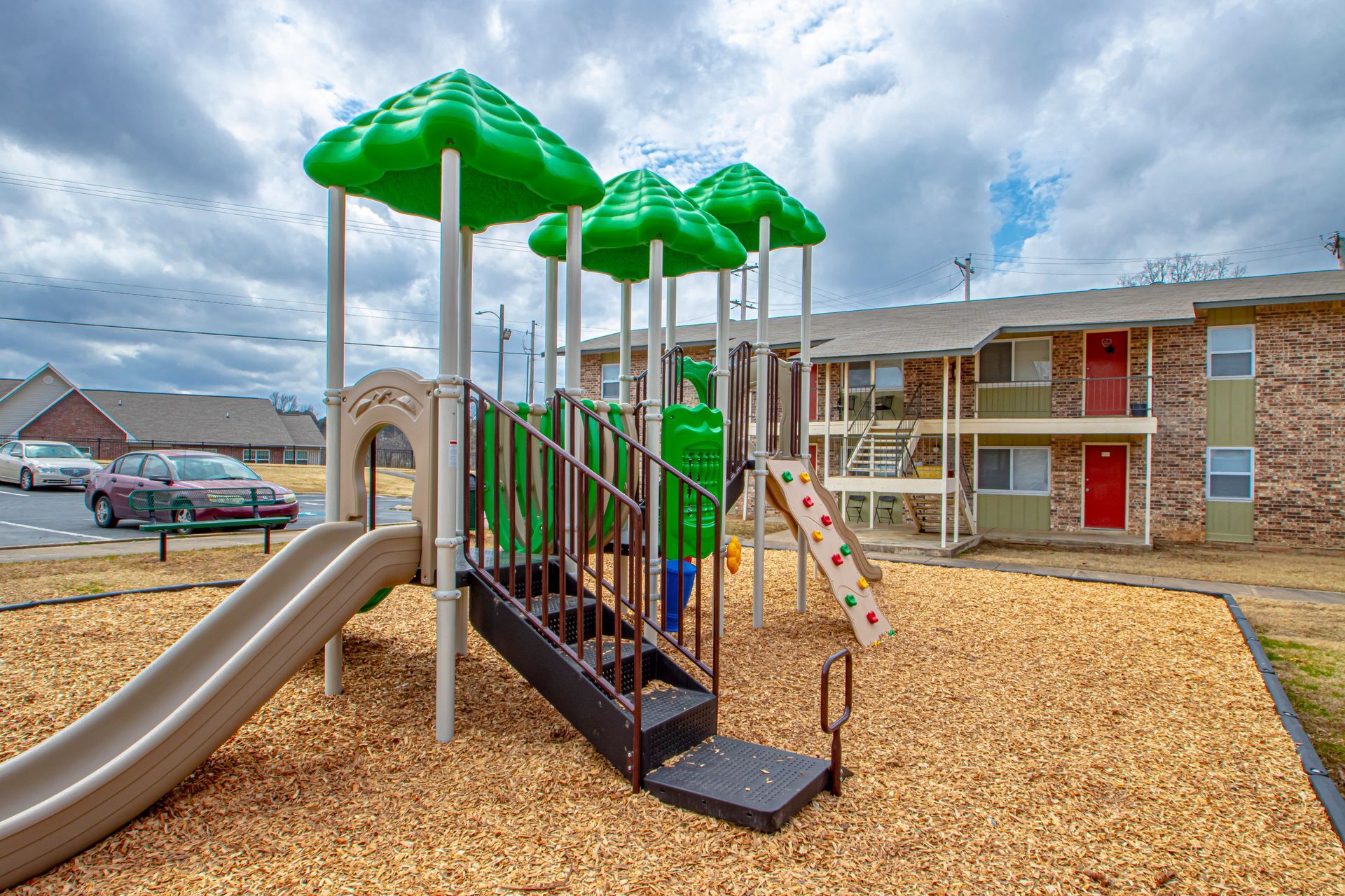 Playground with slides and stairs in front of apartment building; wood chips ground cover.