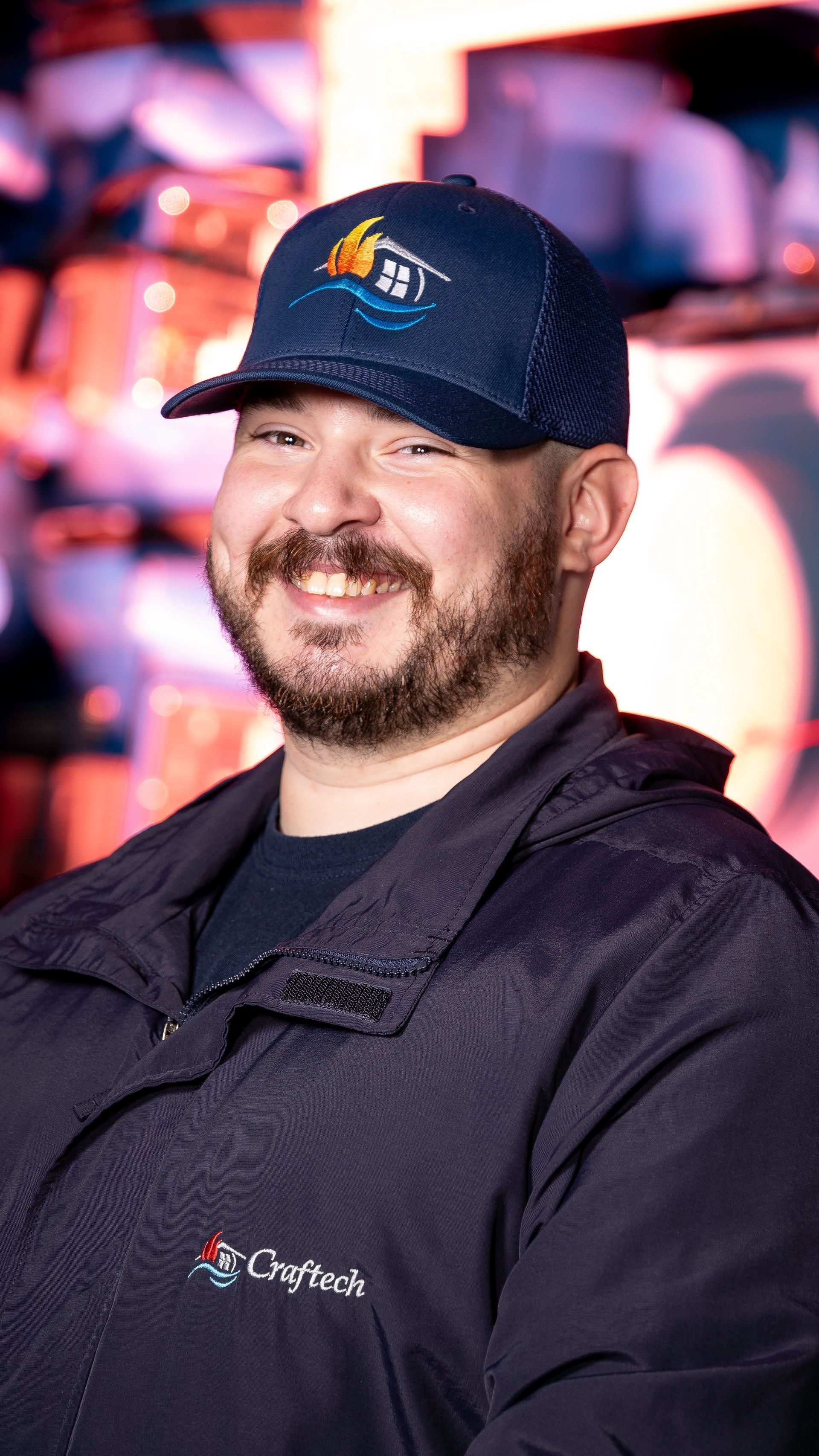 A man with a beard wearing a hat and a jacket is smiling.