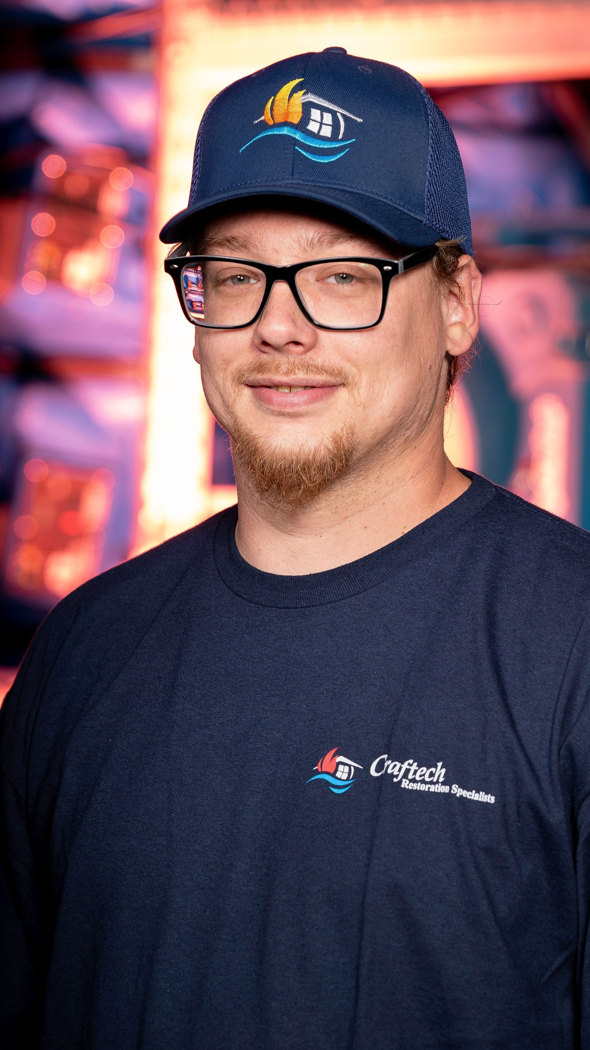 A man wearing a hat and glasses is standing in front of a wall.