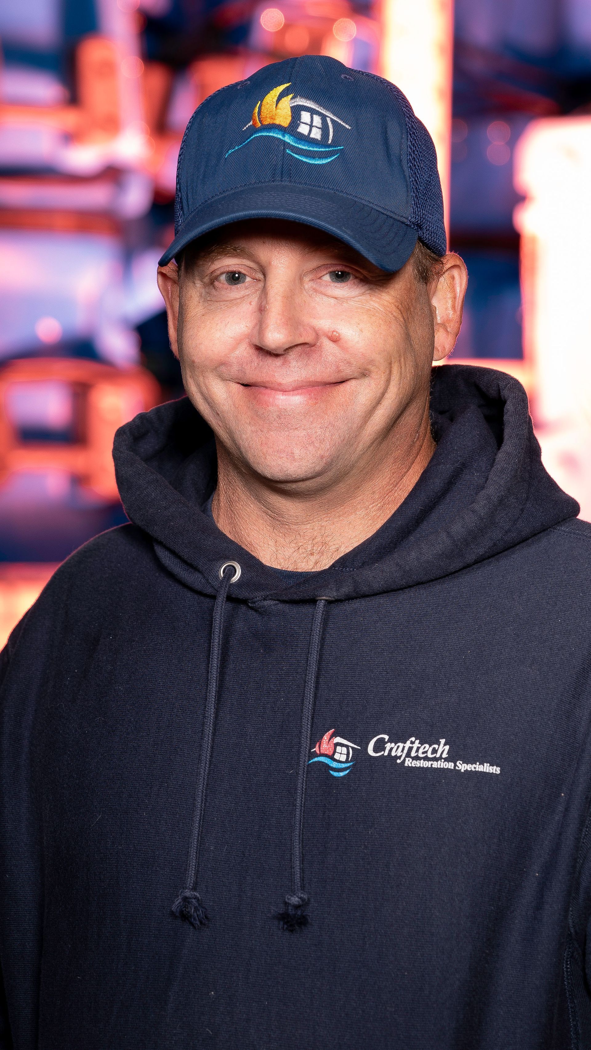 A man wearing a hat and a hoodie is smiling for the camera.