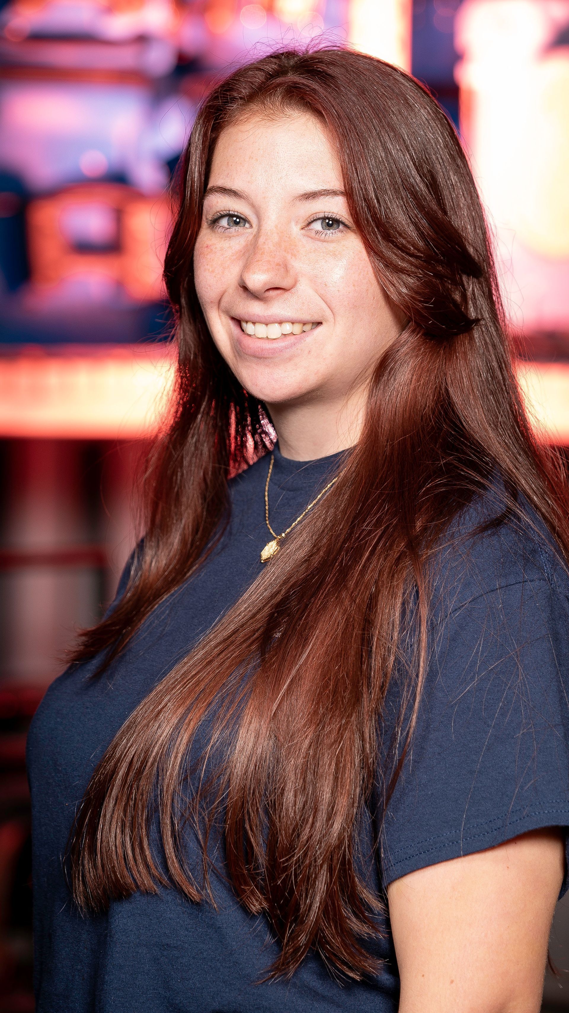 A young woman with long red hair is smiling for the camera while wearing a blue shirt.
