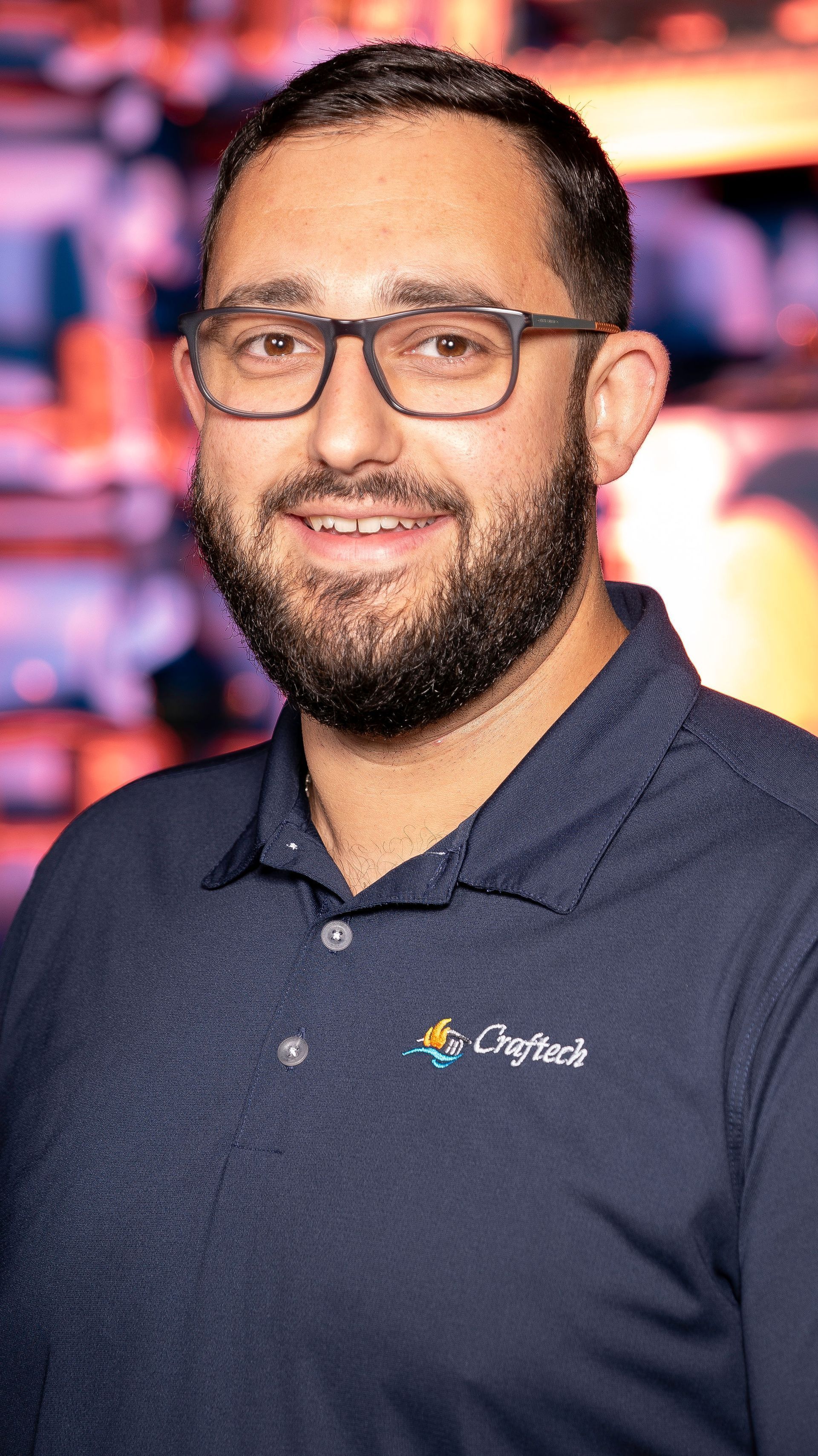A man with a beard and glasses is wearing a blue polo shirt.