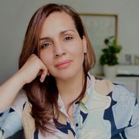 Woman with brown hair resting her hand on her cheek, wearing a patterned shirt, looking at the camera.