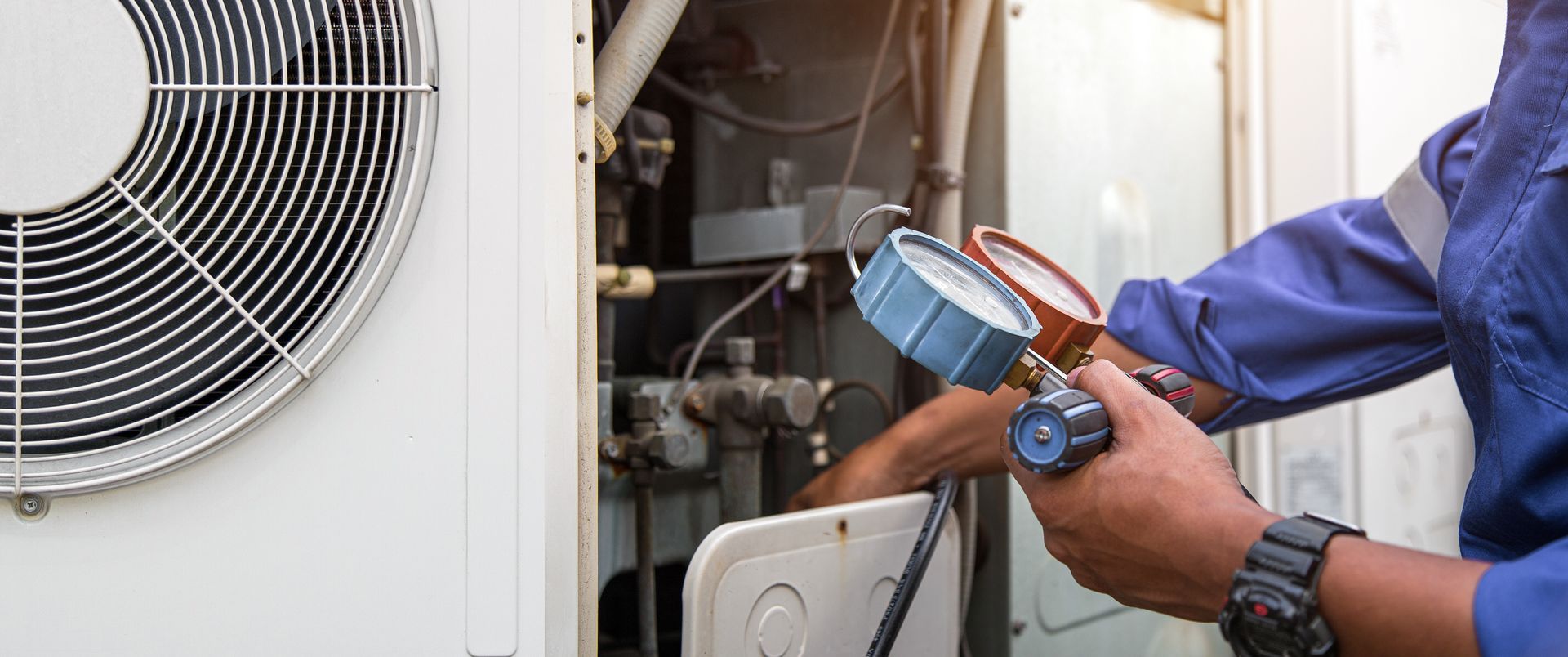 Licensed HVAC tech using a manifold gauge to check refrigerant levels on a residential AC unit