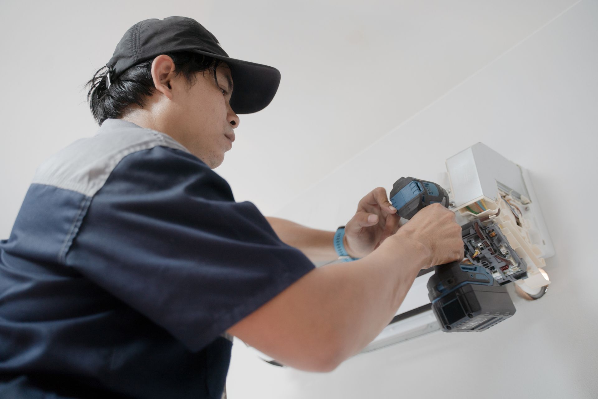 Residential air conditioning contractor fixing a wall mounted air conditioner with a drill.