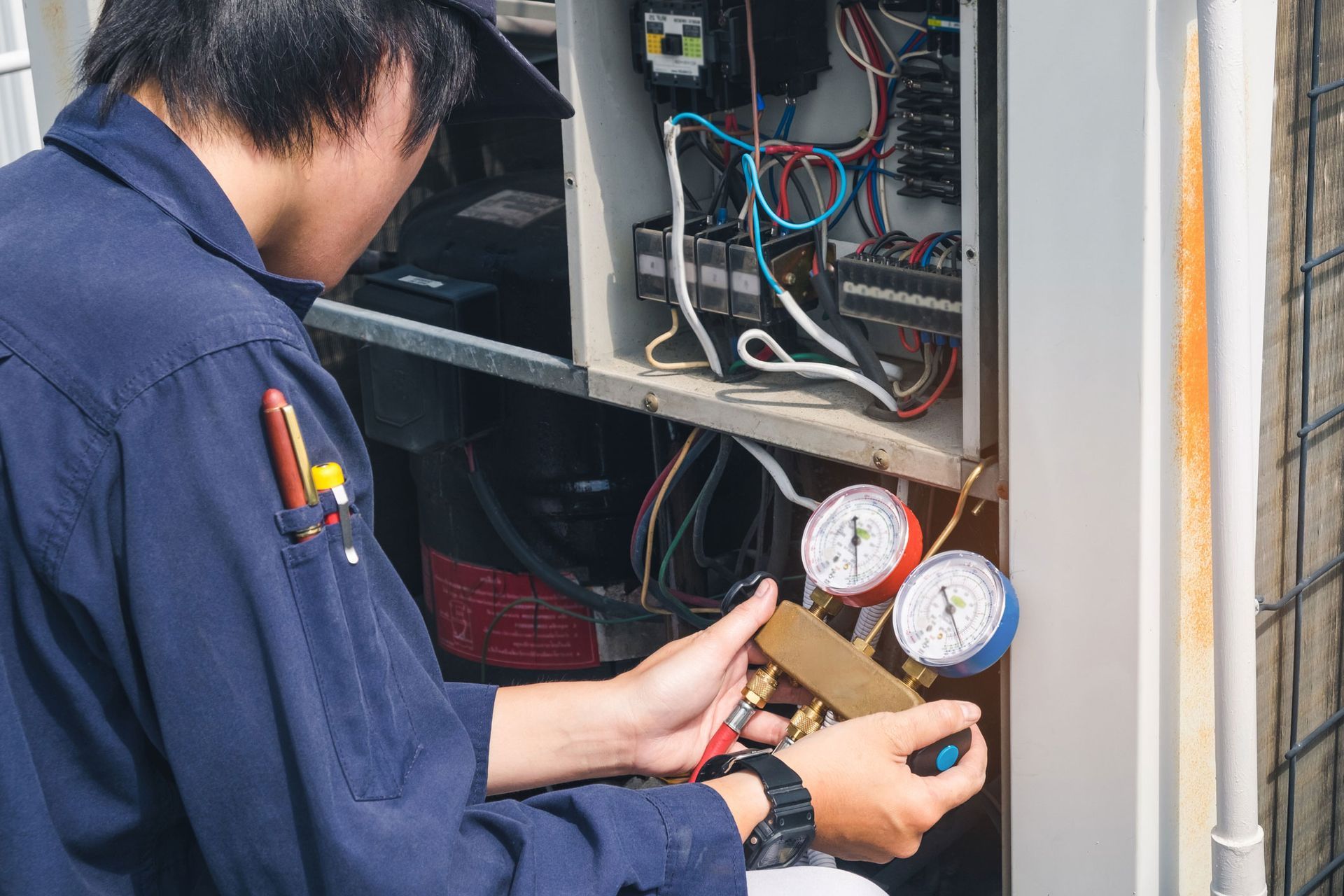 HVAC technician checking refrigerant pressure gauges on air conditioning unit.