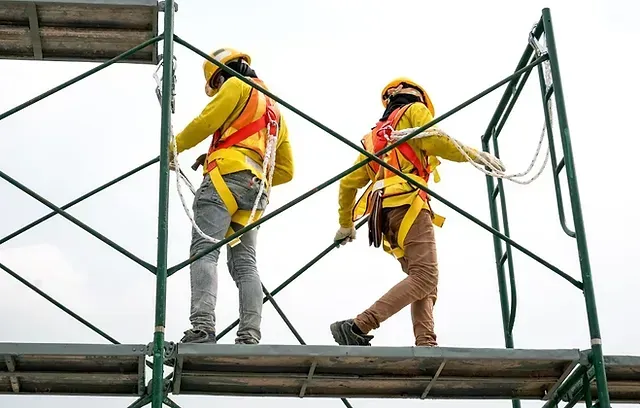Two construction workers are standing on top of a scaffolding.