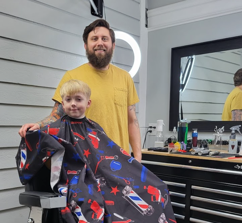 A man is standing next to a little boy in a barber shop.
