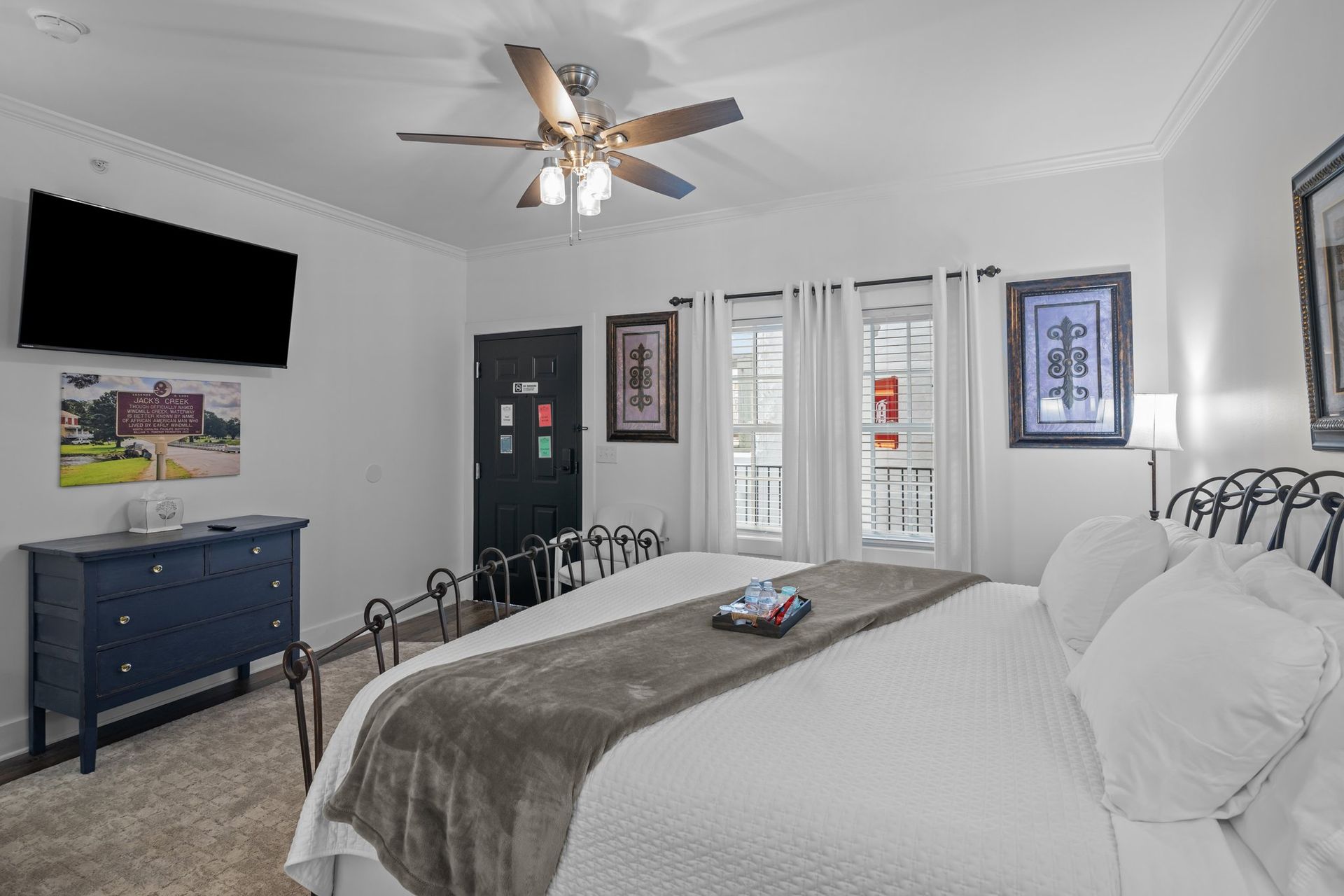 A bedroom with a king size bed , television , dresser and ceiling fan.