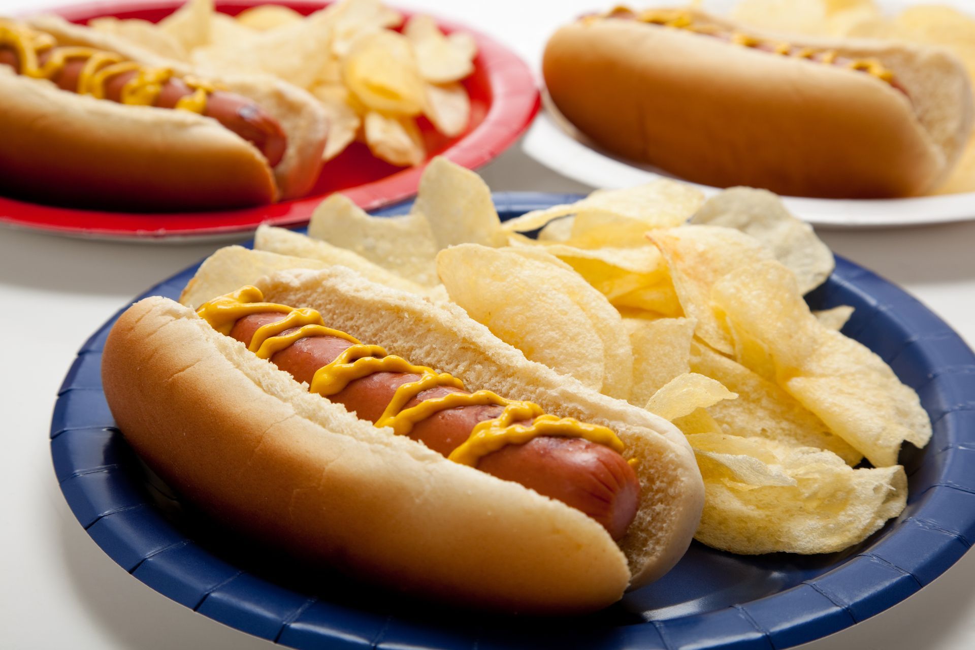 Three plates of hot dogs and potato chips on a table