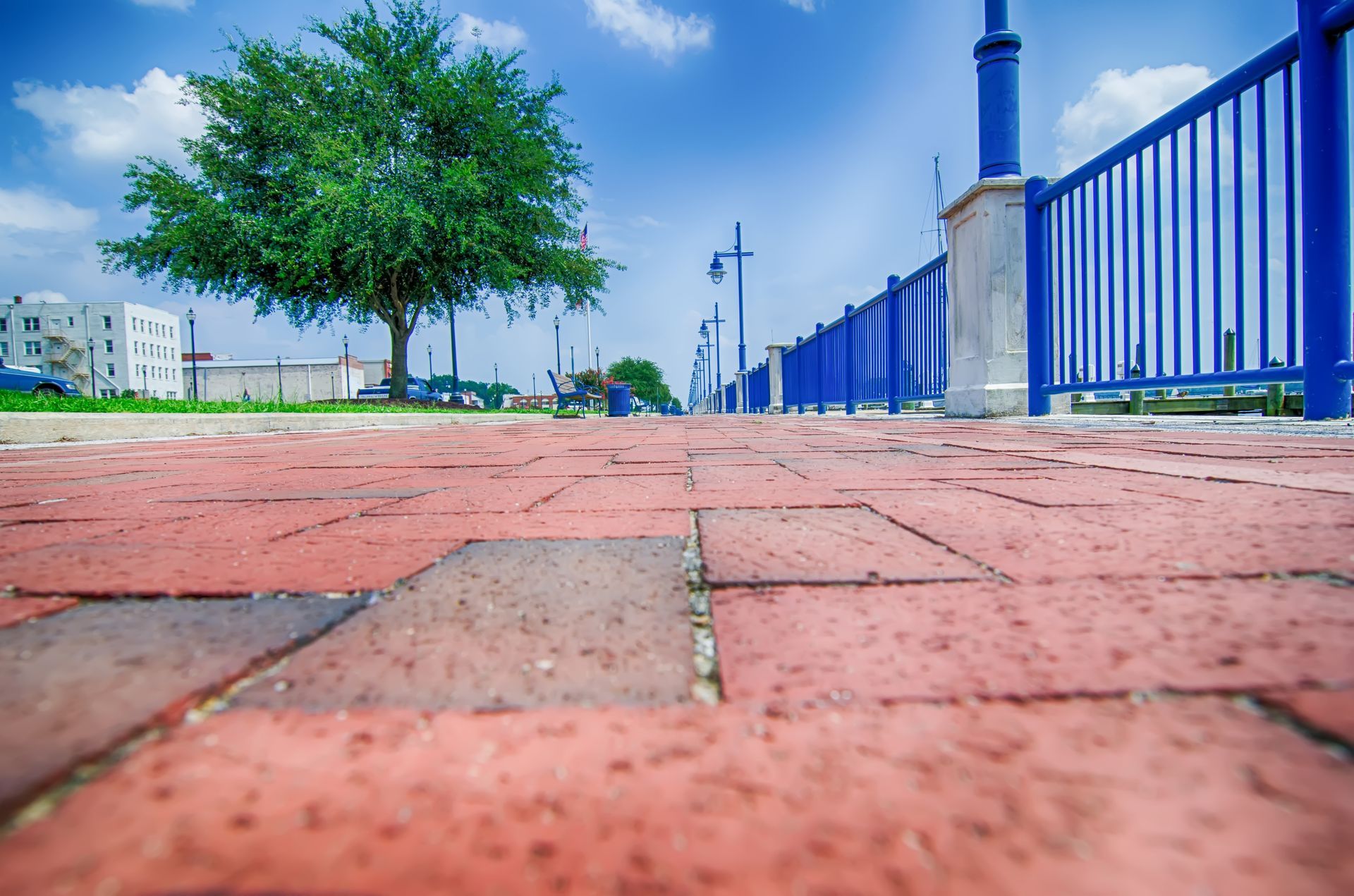 A brick walkway with a blue railing and a tree in the background.