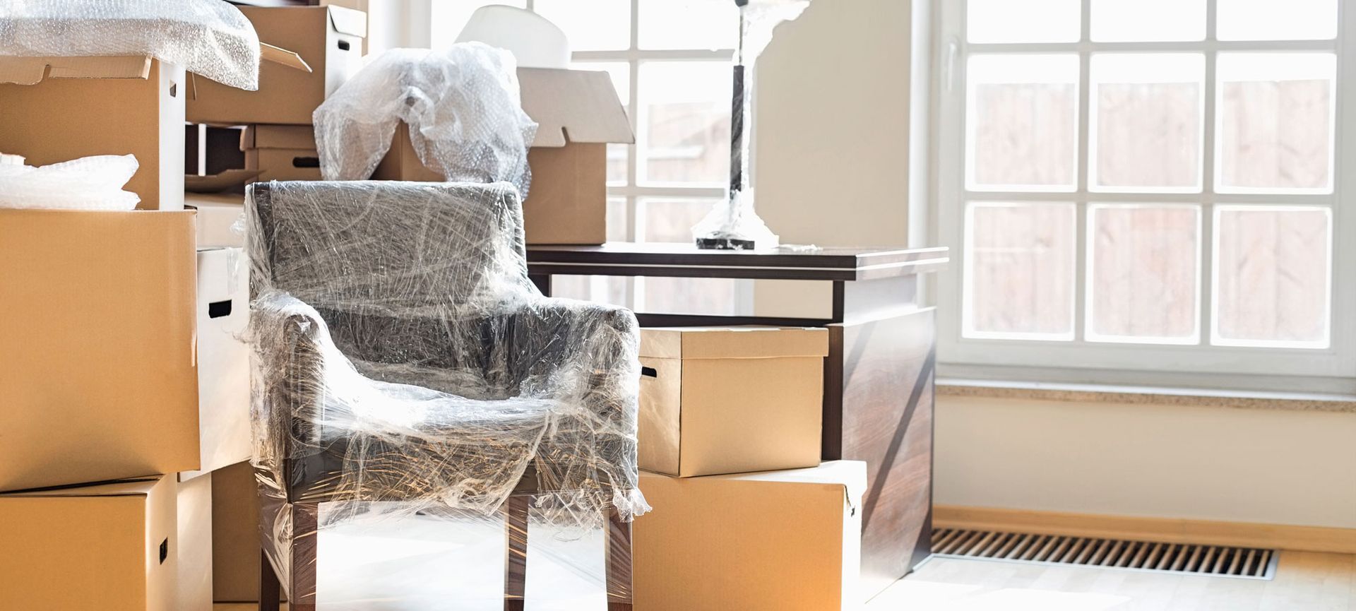 A chair wrapped in plastic is sitting in a room filled with cardboard boxes.