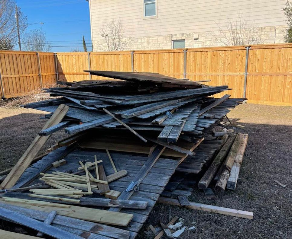 A pile of wood is sitting in front of a wooden fence.