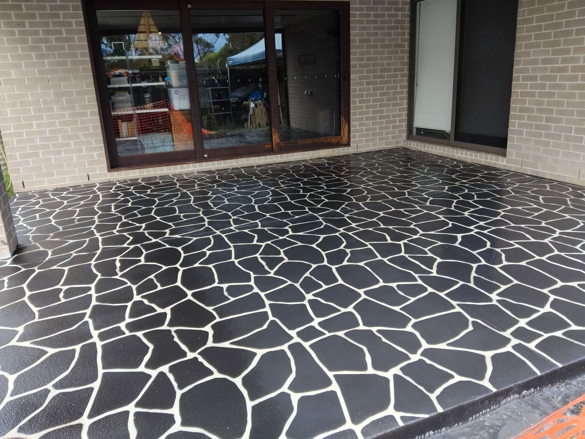 Covered patio with dark stone-patterned floor and sliding glass doors against a brick wall — Troys Concrete Overlays in Hillcrest, QLD